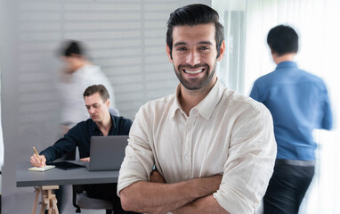 Confidence and happy smiling businessman portrait with blur motion background of his colleague and business team working in office. Office worker teamwork and positive workplace concept. Prudent