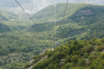 Cable car suspended over a dense forest with mountain and valley views. Aerial journey through nature. Scenic travel in a cable car wagon. City down the hill in a valley. Forest top view.