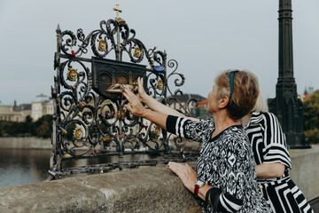 Two women stroke a figurine making a wish on the Charles Bridge.