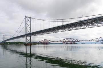 Ship sailing under the red Forth cantilever railway bridge across the Firth of Forth, Queensferry, UK and new Forth Road Bridge crossing in top of image near Edinburgh