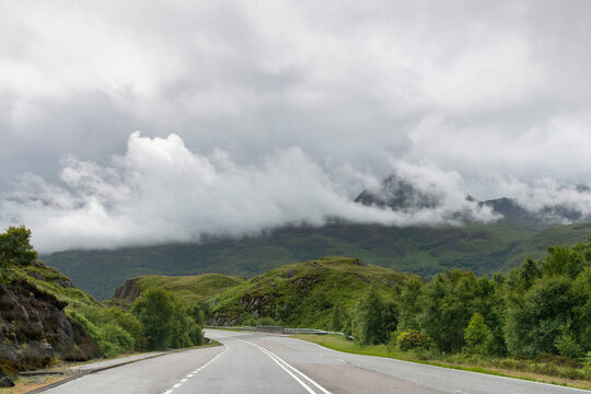 Drivers perspective over the A830 road near Lochailort in Northwest Highlands of Scotland, UK with low hanging light and dark clouds in the green mountains