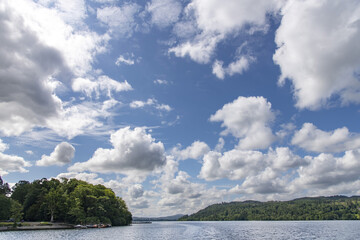 Panoramic cloudscape with view over tranquil waters of a lake with hills with perfect reflection of white cumulus clouds and blue sky in water in Cumbria, England