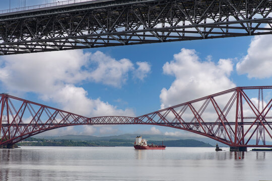 Ship sailing under the red Forth cantilever railway bridge across the Firth of Forth, Queensferry, UK and new Forth Road Bridge crossing in top of image near Edinburgh