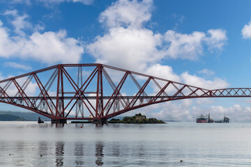 Ship sailing under the red Forth cantilever railway bridge across the Firth of Forth, Queensferry, UK near Edinburgh