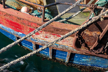Close up of side of a weathered red and blue colored wooden fishing boat with rusted metal...