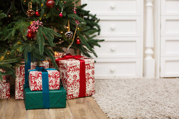 Christmas presents/gifts under fir-tree. Vintage New Year decorations. Red gift boxes and lantern under fir-tree on dark wooden flor. Christmas mood. Celebrating of New Year