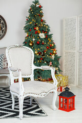 Stylish Christmas light interior with a soft armchair or sofa decorated with garland. Comfort home. Christmas tree with presents underneath in living room