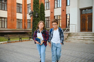 Happy school kids friends boy and girl with backpacks walking and laughing having fun together near school building outside outdoor after lessons