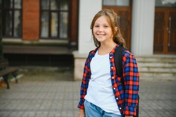 Little schoolgirl with backpack and books near school