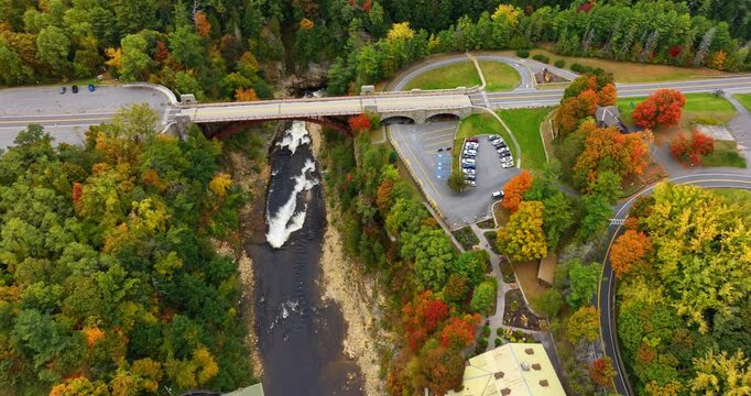 Car goes by the bridge crossing the river flowing in the rocks. Drone footage above the colorful autumn forest in Ausable Chasm in Adirondacks, NY, USA.
