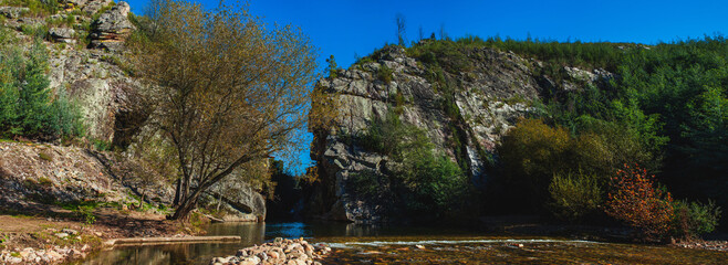 landscape showcases a river flowing between two large rock formations, with towering cliffs on...
