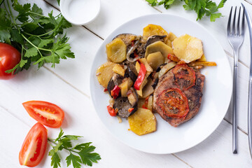 Pork steak with vegetables on a white plate on a white background. Grilled steak and vegetables for lunch. Close-up