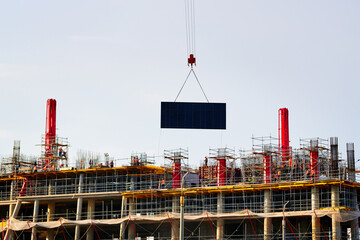 Industrial crane lifting concrete slab at busy construction site with scaffolding and workers, coordination and scale of large urban construction projects. Monolith construction in progress