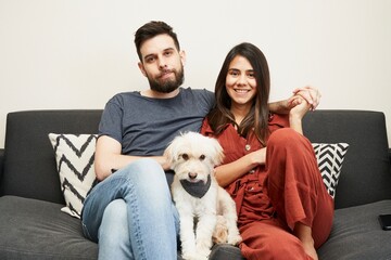 Joven pareja sonrientes sentados en el sofá con su mascota