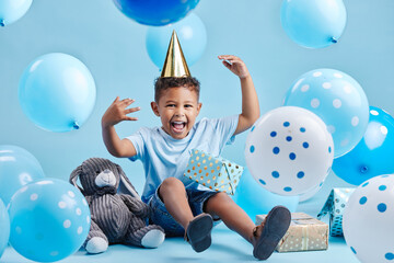 Boy, child and balloons for birthday party in studio portrait with present, happy or bunny doll by...