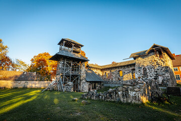 Fototapeta premium A historic stone fortress featuring wooden towers and platforms under a clear sky. Autumn foliage adds vibrant orange hues, enhancing the rustic charm of the ancient architecture.