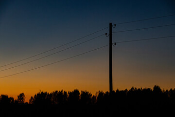 A minimalist scene featuring a power line silhouette with trees in the distance, set against a gradient sunset sky transitioning from orange to deep blue.