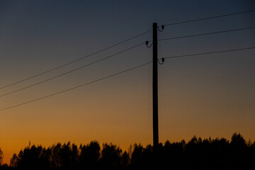 A minimalist scene featuring a power line silhouette with trees in the distance, set against a gradient sunset sky transitioning from orange to deep blue.