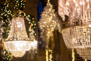 Elegant chandeliers adorned with sparkling crystals illuminate a festive hall, surrounded by twinkling holiday lights