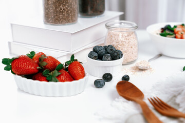 Presented by fruits putting yogurt toppings with strawberry, berry, oats, raisins and chia seed decorated by peppermint in white blow. Pink background. Set of healthy dairy product choice. Pecuniary.