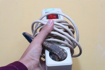 A person's hand is grasping a dirty, white power strip with a tangled, off-white cord, revealing...