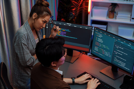 IT developers discussing with point to intelligent website development coder system running data online on pc of two screens with information technology at neon light room at modern office. Infobahn.