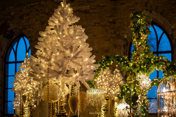 Elegant winter decor featuring a white Christmas tree adorned with lights in a beautifully lit interior space during twilight. Background with Luxurious Christmas decorations and crystal chandeliers