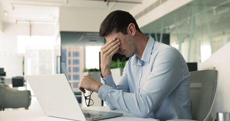 Young businessman sit at desk with laptop takes off eyeglasses to reduce eyestrain, discomfort, looks exhausted, frustrated with bad news, feeling work-related stress, missed deadline, health issues
