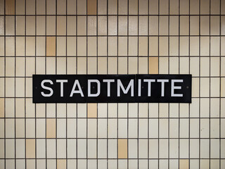 Stadtmitte sign at the underground train station in Berlin Mitte, Germany. Location name of the public transportation. Beige tiled wall with white letters on black.