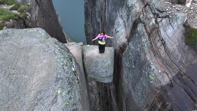 Girl Adventurist is Jumping on Kjeragbolten in Norway. Kjerag Boulder in Mountains Fjord Landscape Aerial view.