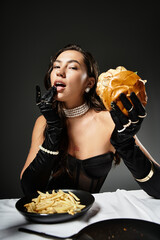 A young woman dressed elegantly indulges in a gourmet burger and fries while exuding confidence.