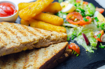 A plate of food with a sandwich, cheese sticks, and ketchup
