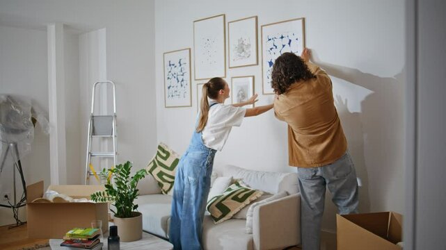 Couple hanging pictures wall apartment. Happy woman and man enjoy collaborating 