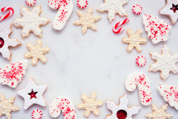 Christmas baking frame with an assortment of red and white theme cookies and candies. Top down view on a white marble background with copy space. Holiday candy cane baking concept.