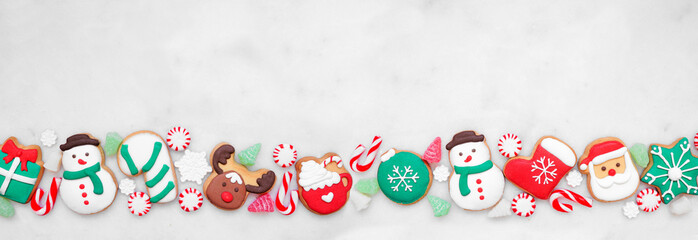 Cute colorful Christmas cookie bottom border on a white marble banner background with copy space. Top view. Holiday baking concept.