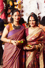 Two joyful Indian women in traditional sarees performing the Bengali ritual 