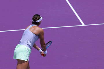 Tennis pro preparing to write a serve, on a purple concrete court.