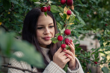 The girl holds in her hands a branch of an apple tree with red apples.