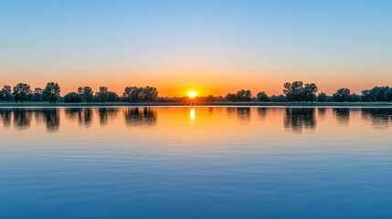 Fototapeta premium A beautiful sunset casts warm colors over a tranquil lake. Trees line the shore, reflecting in the still waters as the sun sinks below the horizon, creating a peaceful atmosphere