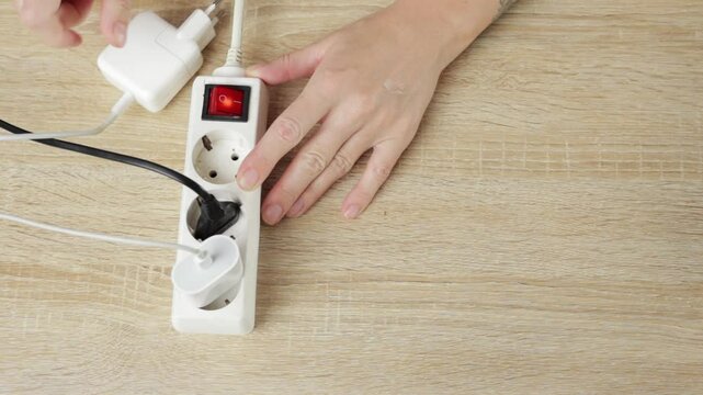 Woman Hand Close Up Connects and Disconnects Various Plugs and Adapters From Power Strip on Wooden Table, Illustrating Interactions with Electrical Devices and Power Management
