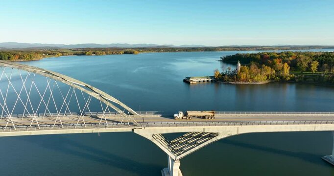 Aerial view of Lake Champlain Bridge during autumn, spanning the serene lake and connecting Crown Point, New York to Vermont, with fall foliage and distant mountain ranges under clear skies.