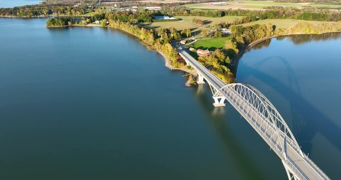 Aerial view of Lake Champlain Bridge during autumn, spanning the serene lake and connecting Crown Point, New York to Vermont, with fall foliage and distant mountain ranges under clear skies.