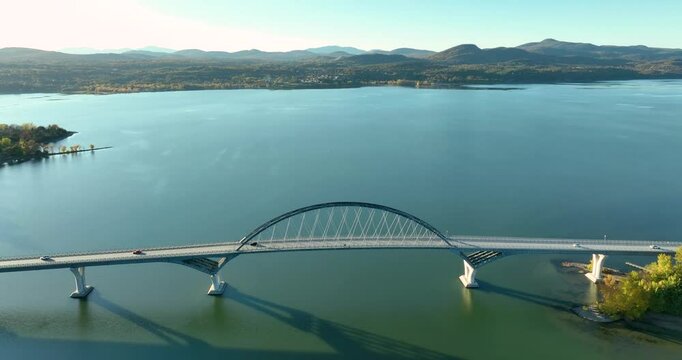 Aerial view of Lake Champlain Bridge during autumn, spanning the serene lake and connecting Crown Point, New York to Vermont, with fall foliage and distant mountain ranges under clear skies.