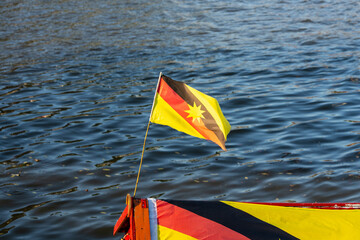 Sarawak flag with rough tatty edges blowing in breeze, on flag pole attached to boat with...