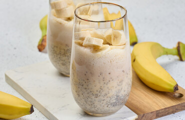 Glass with chia and yogurt dessert garnished with fresh banana slices on white table