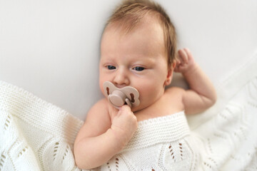 Adorable newborn relaxing with pacifier wrapped in soft blanket. High quality photo