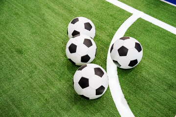 On a vibrant and lush green soccer field, you can see three shiny soccer balls perfectly placed on the surface, eagerly waiting for an exciting game of soccer to begin at any moment now © Aleksey