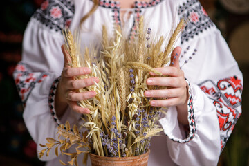 a woman in an embroidered dress holds ears of wheat