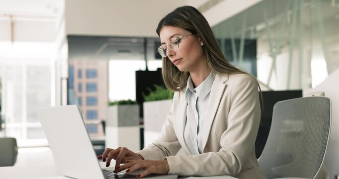 Young serious woman using laptop at modern workplace, performing administrative tasks, accessing company database, prepare contract for signing, editing legal documents, updating on-line information