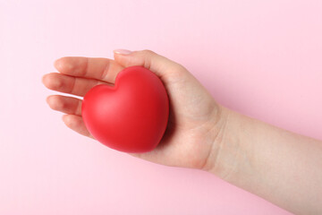 Fototapeta premium Woman holding red heart on pink background, top view